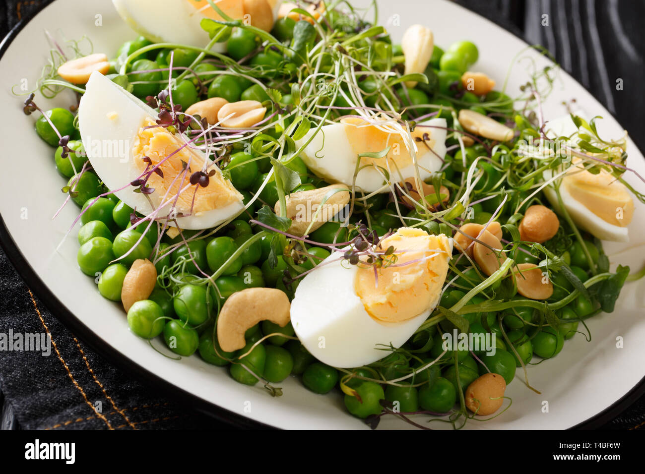 Leckeren, gesunden Salat von grünen Erbsen, micro Grüns, Nüsse und Eier close-up auf einem Schild auf dem Tisch gekocht. Horizontale Stockfoto