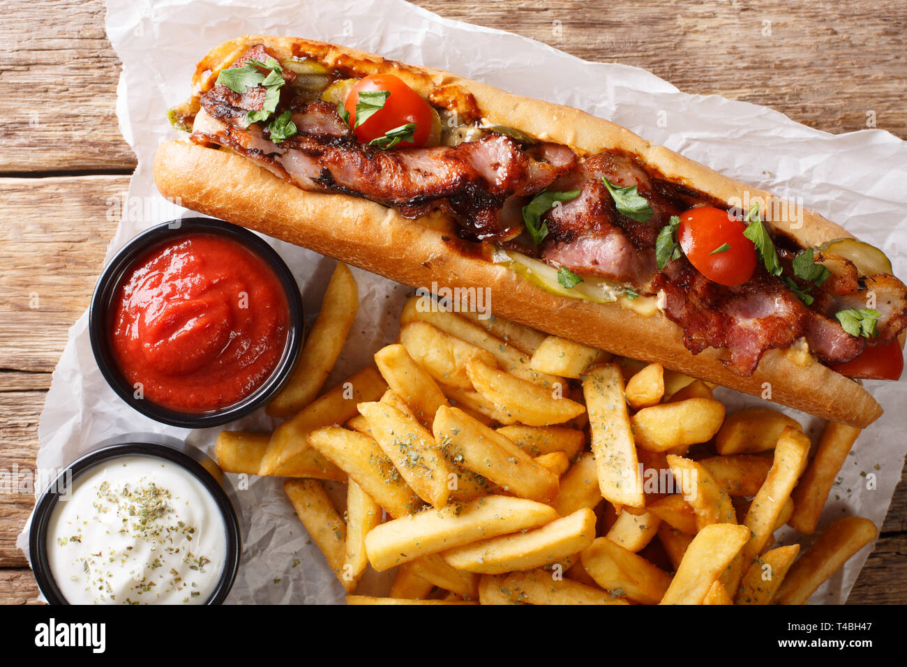 Lecker Hot Dog mit Speck und Gemüse mit Pommes frites und Saucen in der Nähe serviert - auf den Tisch. horizontal oben Ansicht von oben Stockfoto