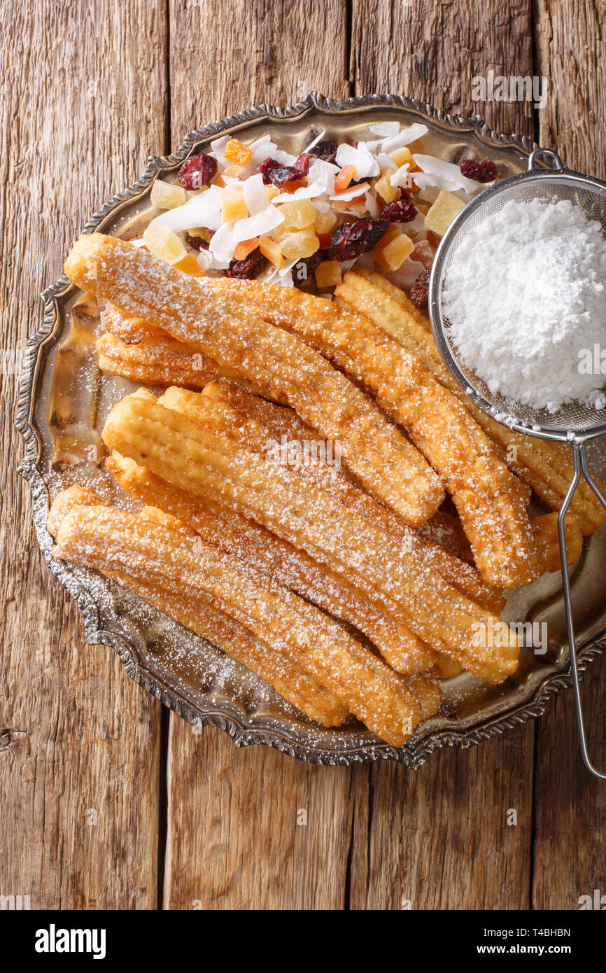 Leckere hausgemachte Churros mit Puderzucker und kandierten Früchten close-up auf den Tisch. Vertikal oben Ansicht von oben Stockfoto