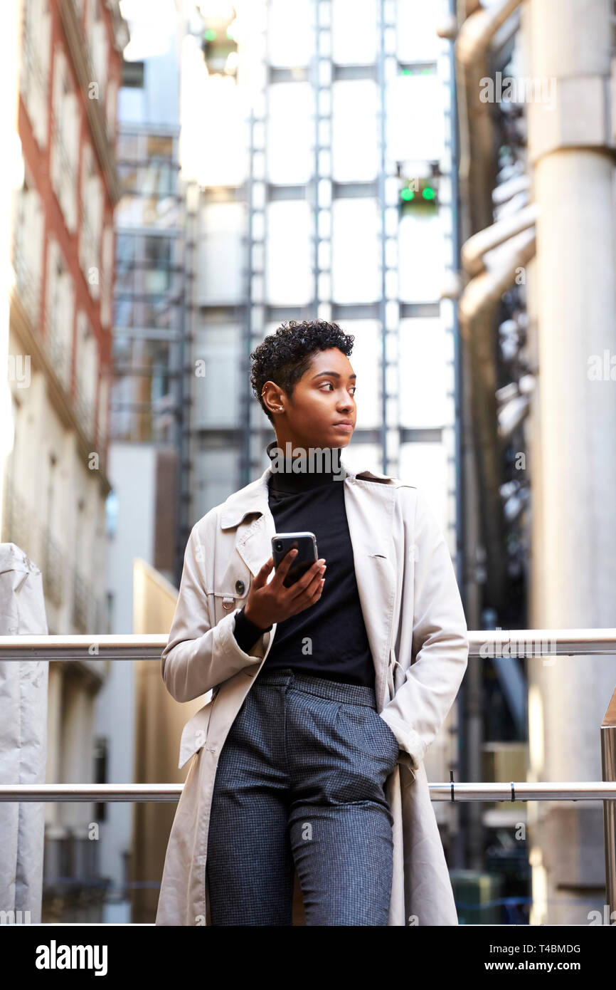 Modische junge schwarze Frau Schiefen auf Handlauf in der Stadt halten, Smartphone, niedrigen Winkel, Nahaufnahme, vertikal Stockfoto