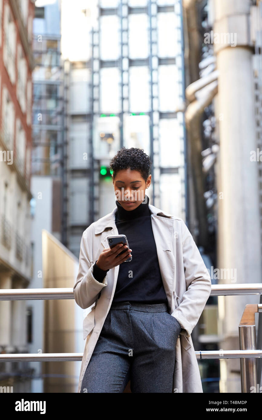 Modische junge schwarze Frau, die in der Stadt lehnte sich auf eine Hand über ihr Smartphone, vertikalen Schiene Stockfoto
