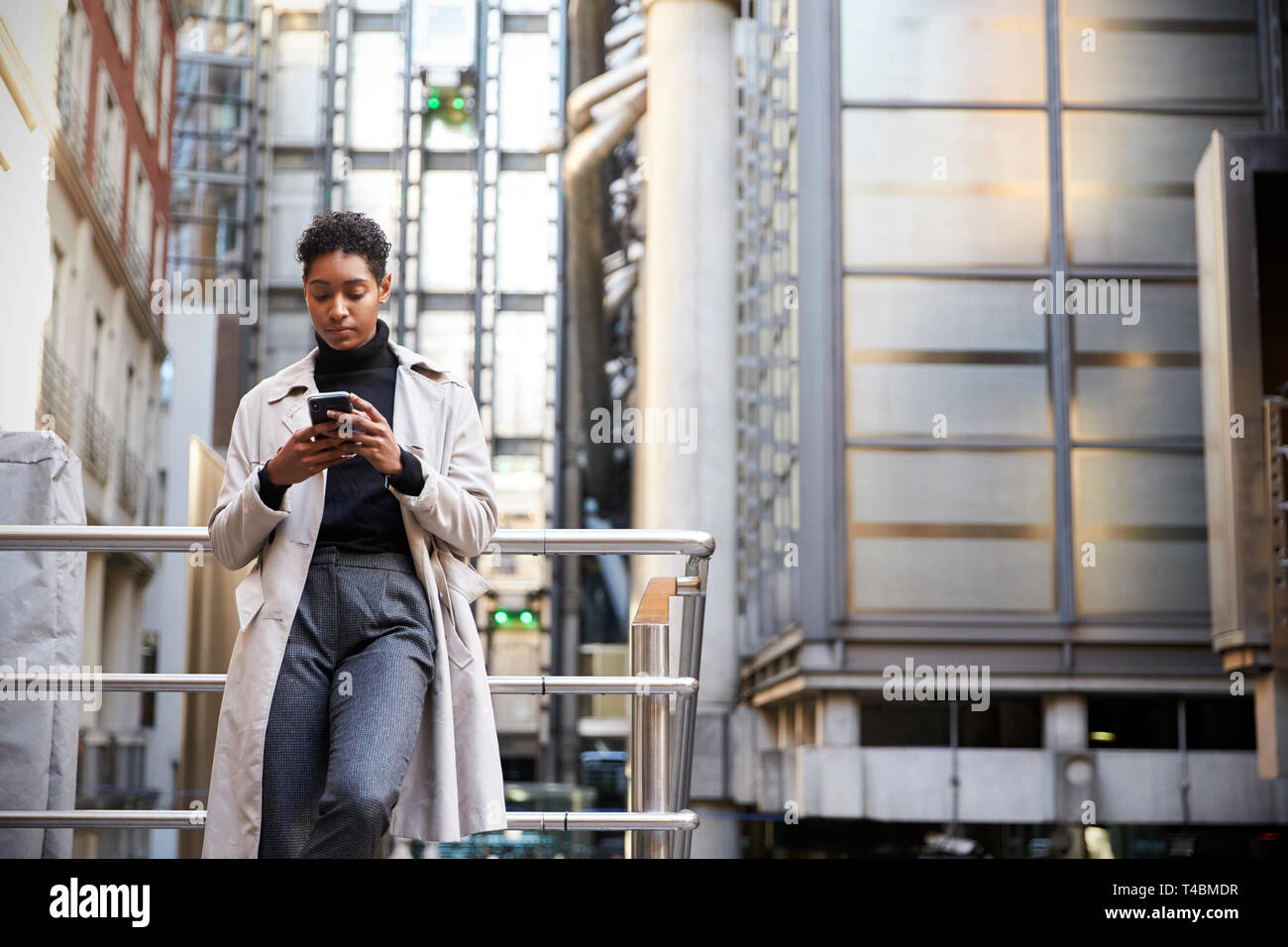 Modische junge schwarze Frau, die in der Stadt lehnte sich auf eine Hand über ihr Smartphone, niedrigen Winkel Schiene Stockfoto