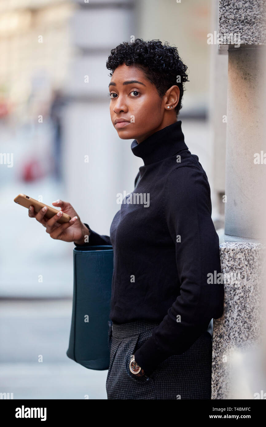 Junge erwachsene Frau auf einer Straße in London stehen mit ihrem Smartphone und Wegsehen, selektiver Fokus Stockfoto