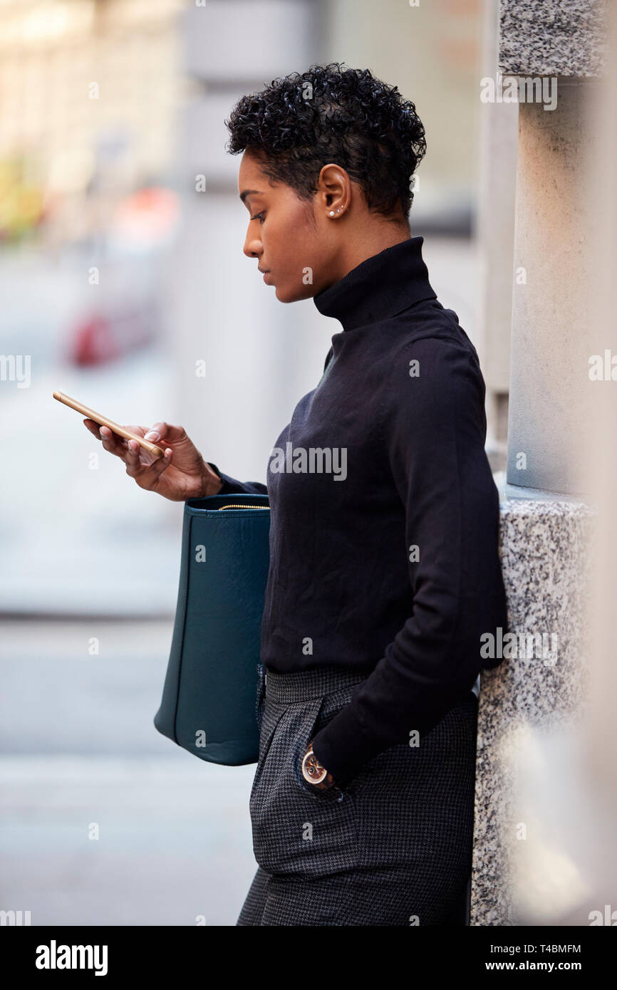 Junge schwarze Frau, die auf einer Straße in London können Sie über ihr Smartphone, Seitenansicht, Nahaufnahme, vertikal Stockfoto