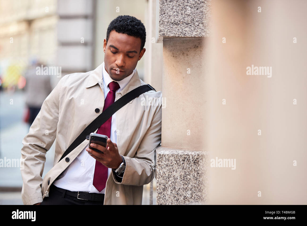 Junge schwarze Geschäftsmann lehnte sich an eine Wand in der Straße in London mit Smartphone, selektiver Fokus Stockfoto