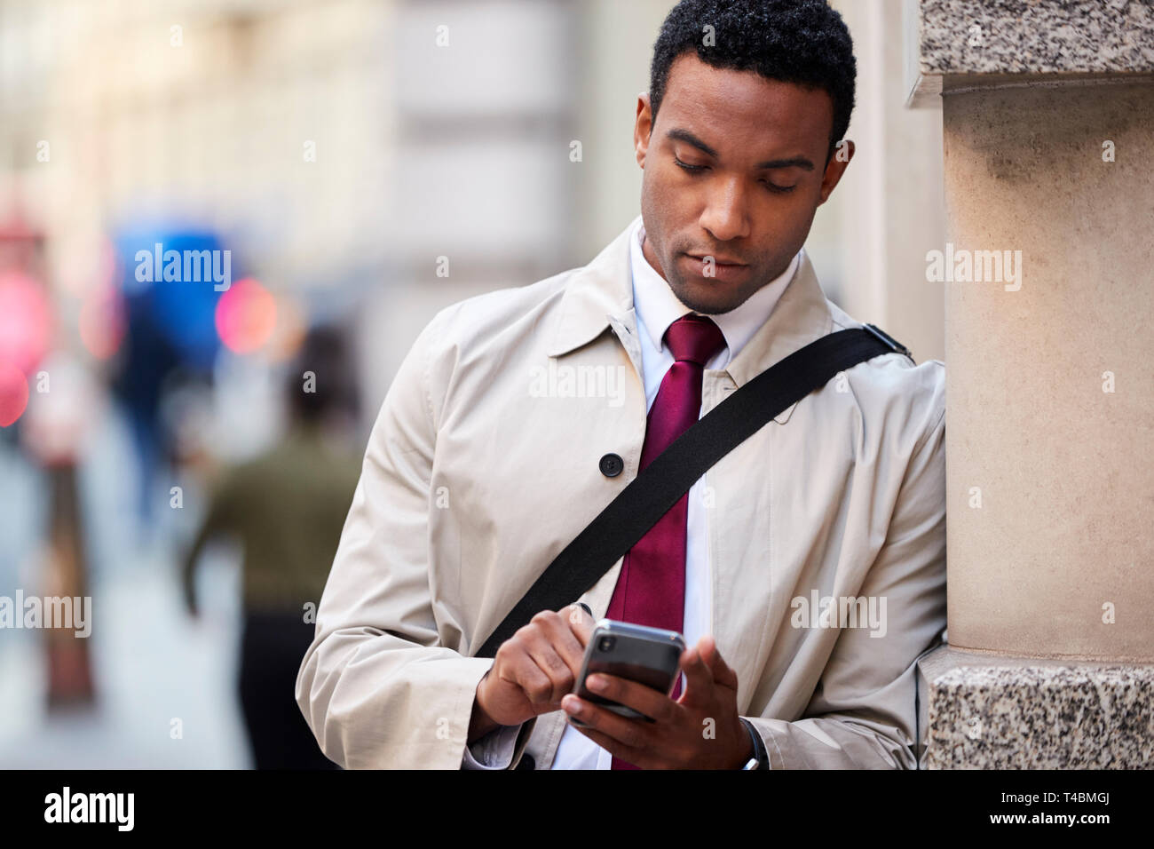 Junge schwarze Geschäftsmann lehnte sich an eine Wand in der Straße in London mit Smartphone, selektiver Fokus, Nahaufnahme Stockfoto