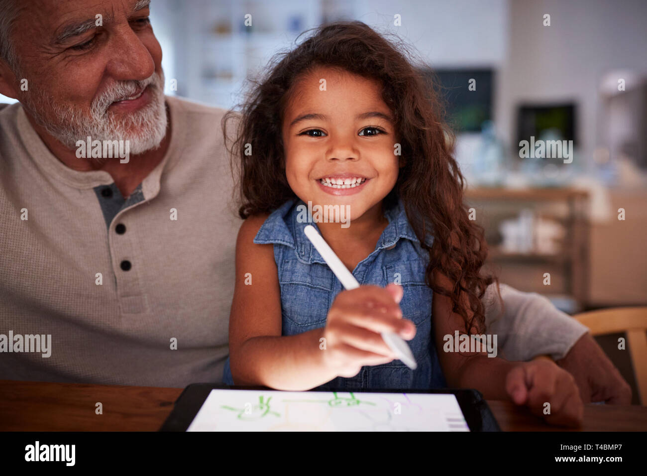 Senior Hispanic Mann mit seiner jungen Enkelin mit Stift und Tablet Computer, lächelnd in die Kamera Stockfoto