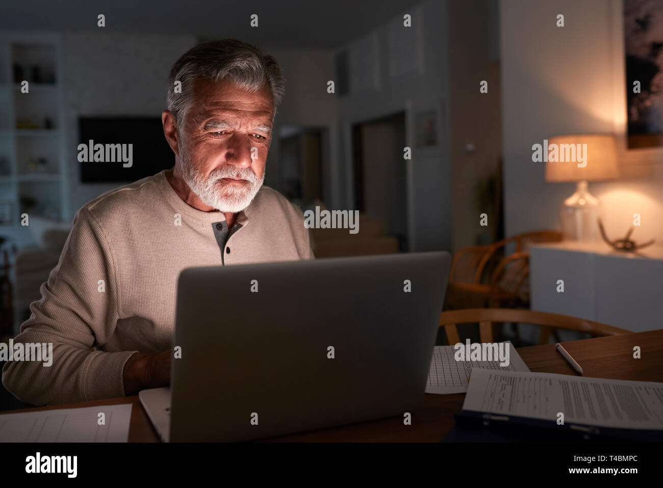 Senior Hispanic Mann seine Finanzen Prüfung online zu Hause mit einem Laptop in der Nacht Stockfoto