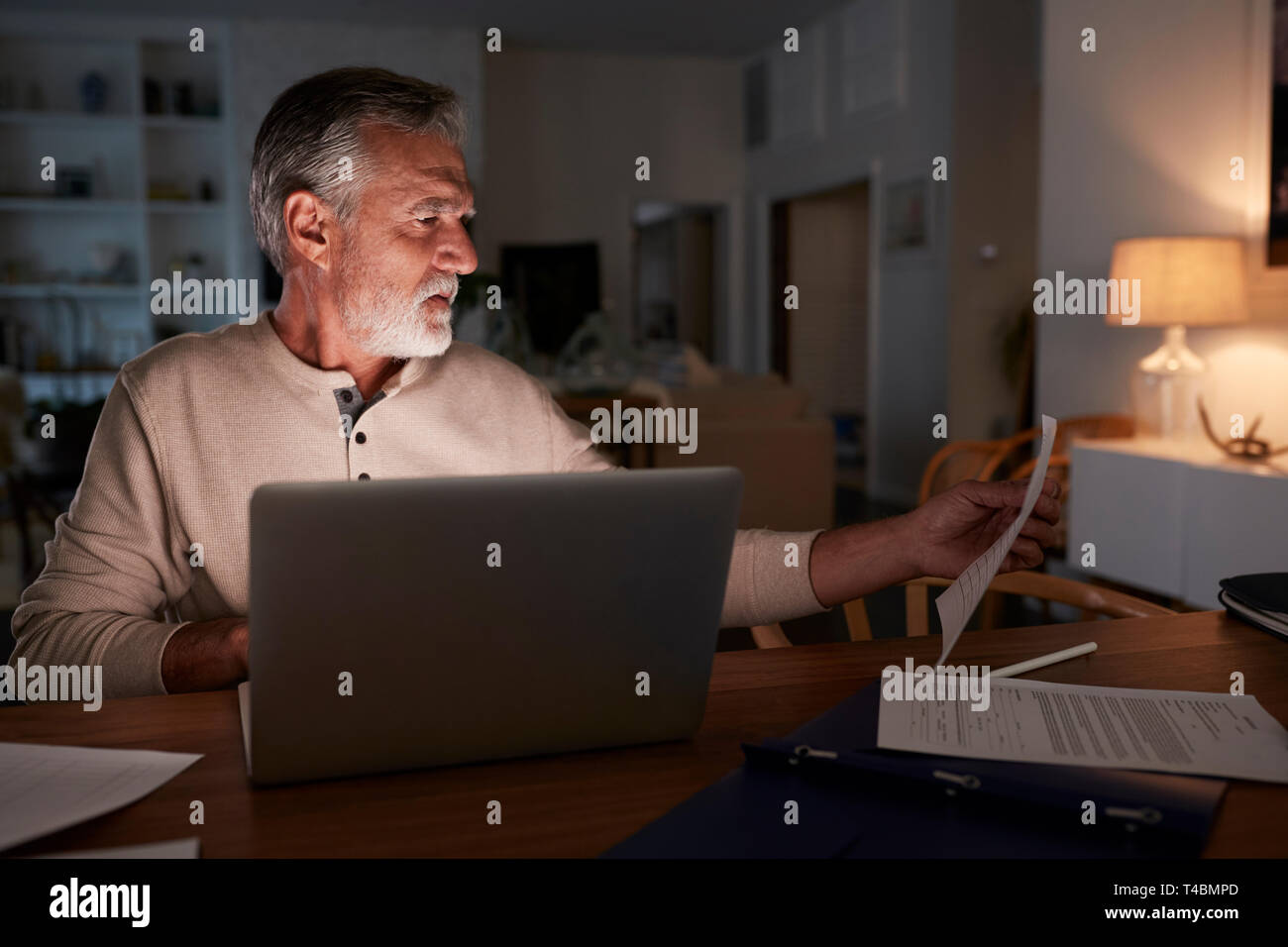 Senior Hispanic Mann seine Finanzen Prüfung online zu Hause mit einem Laptop in der Nacht Stockfoto