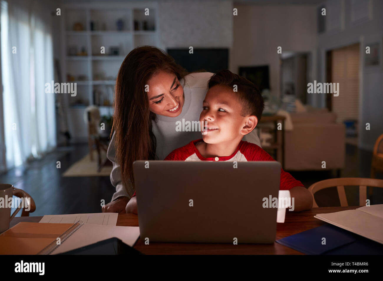 Hispanic Frau schaut über die Schulter ihres Sohnes, während er seine Hausaufgaben mit Laptop Stockfoto