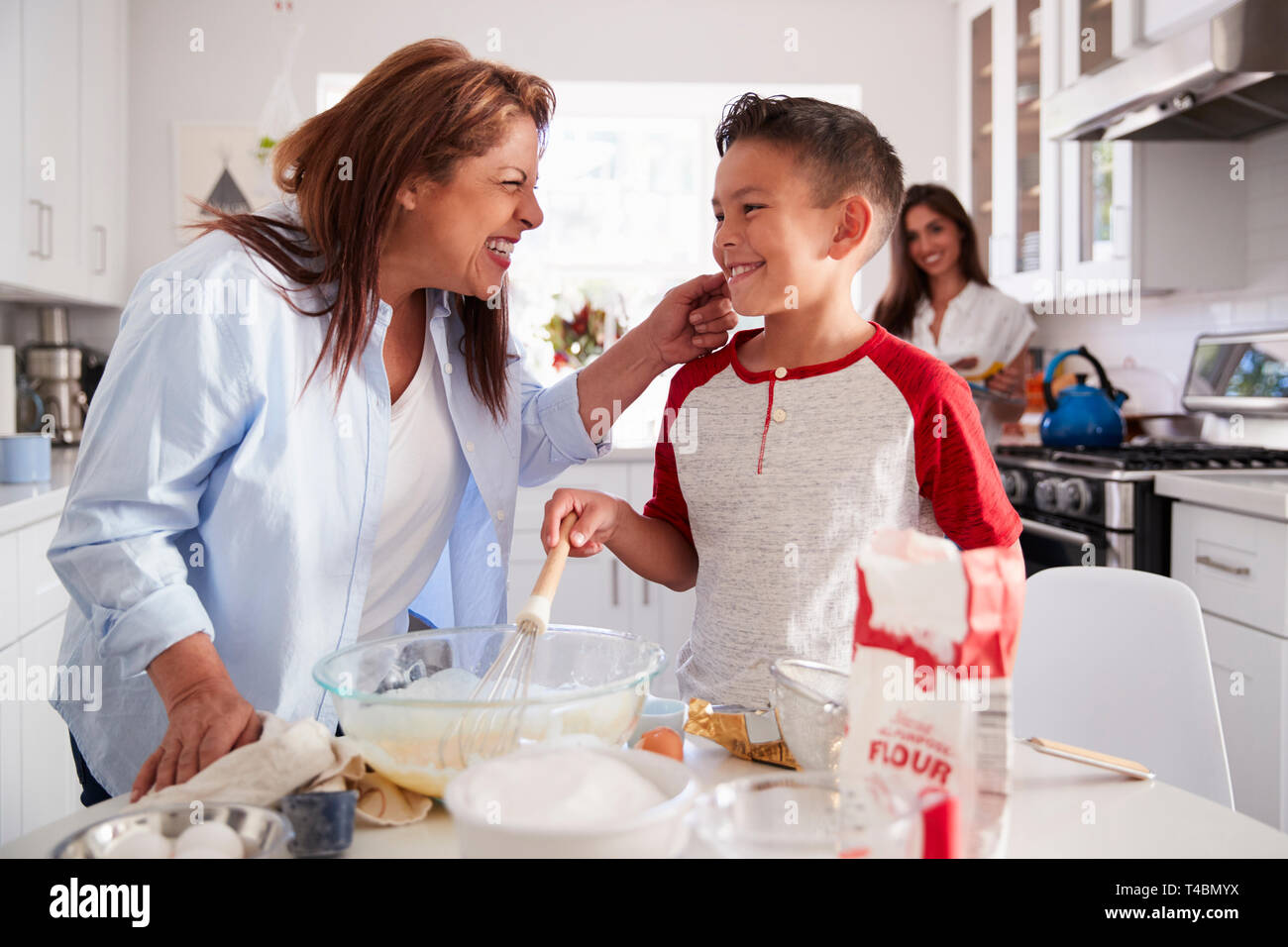 Pre-teen Boy einen Kuchen in der Küche mit seiner Großmutter, seine Mutter steht im Hintergrund Stockfoto