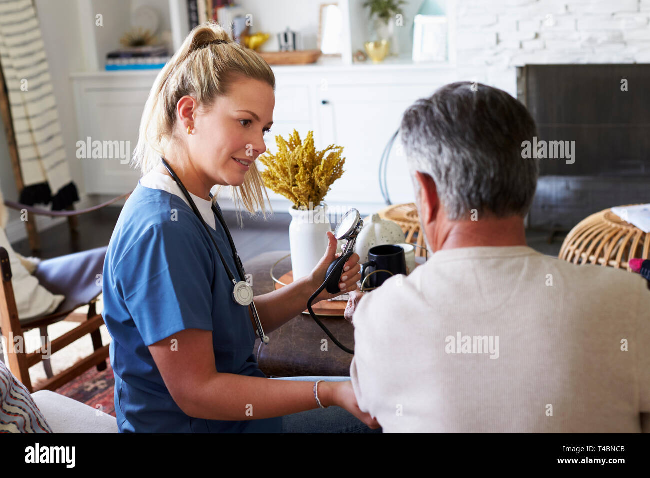 Zurück Blick auf weibliche Arbeitnehmer im Gesundheitswesen messen den Blutdruck der älteren Mann während eines Home Besuch Stockfoto