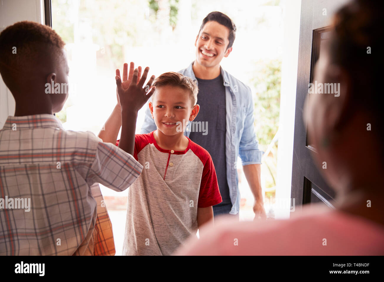 Die beiden Pre-teen Boys High Five in die offene Tür, wie Vati läßt seinen Sohn im Haus seiner Freunde Stockfoto