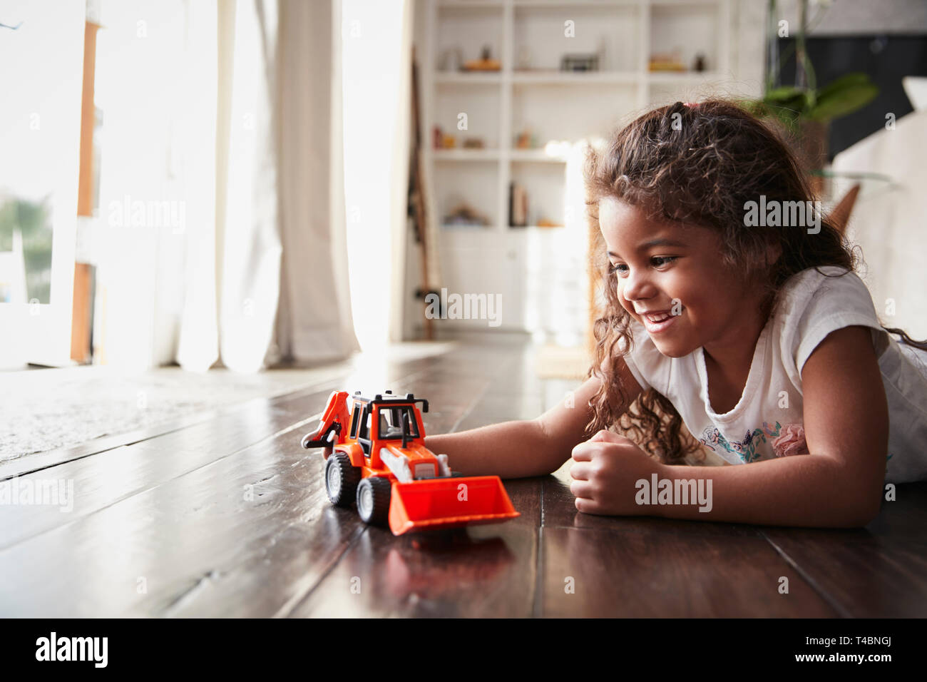 Junge Hispanic Mädchen liegt auf dem Fußboden im Wohnzimmer spielen mit einem Spielzeug bagger Stapler Stockfoto