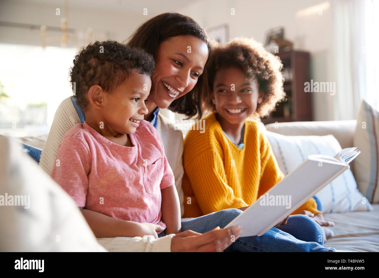 Nahaufnahme der jungen Mutter sitzt auf einem Sofa im Wohnzimmer ein Buch lesen, um ihre beiden Kinder, Nahaufnahme, Seitenansicht Stockfoto
