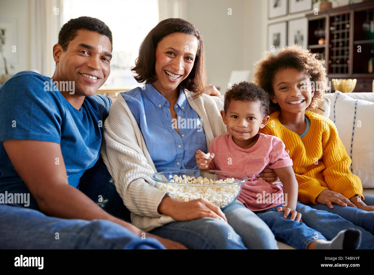 Jungen gemischten Rennen Familie sitzen zusammen auf dem Sofa im Wohnzimmer, essen Popcorn und Blick in die Kamera, Vorderansicht Stockfoto