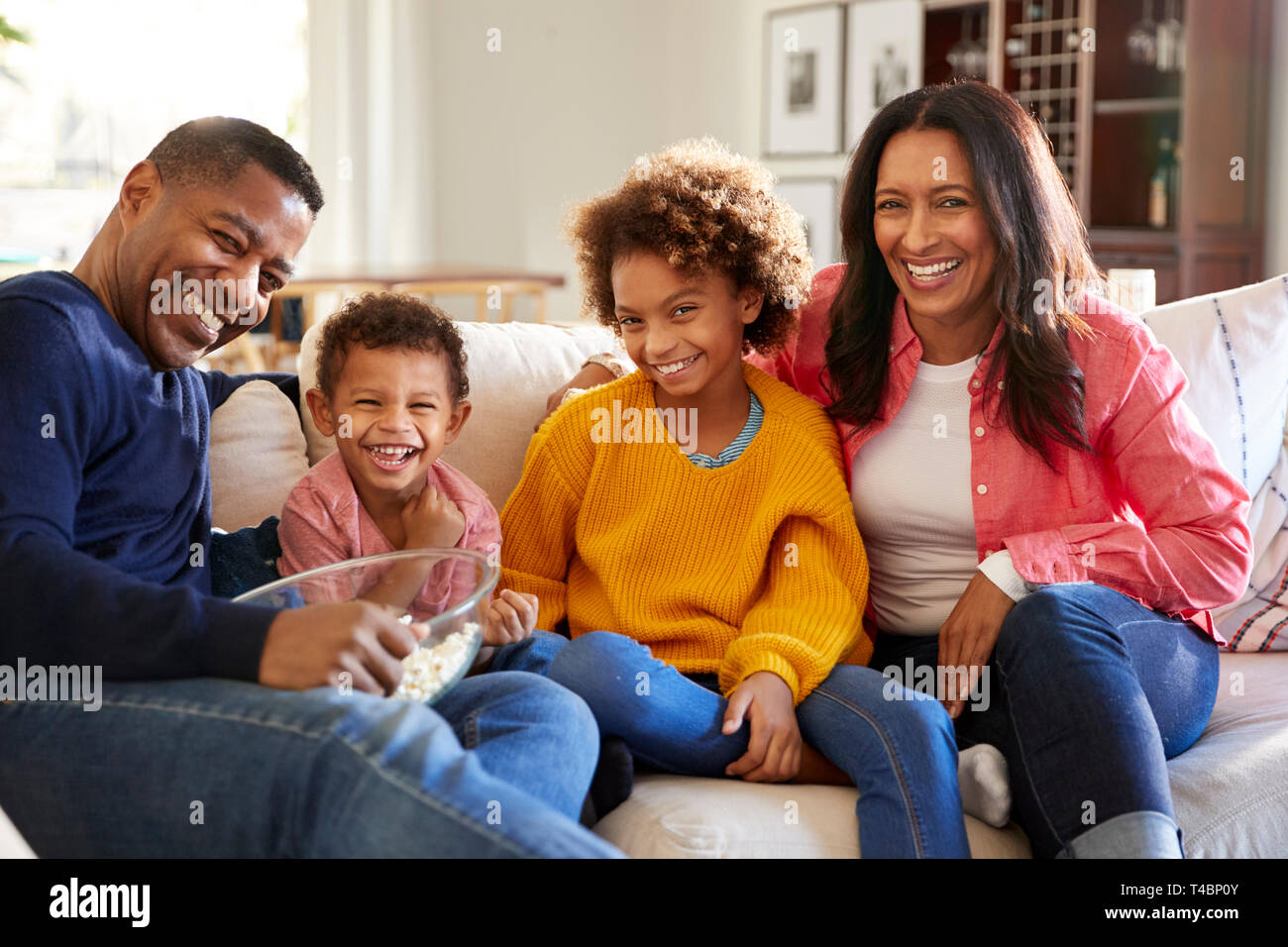 Junge Großeltern mit ihren Enkelkindern auf dem Sofa im Wohnzimmer essen Popcorn und Lachen, Vorderansicht, in der Nähe Stockfoto