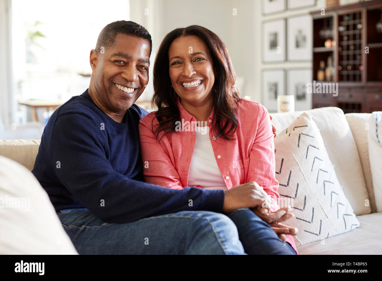 Mittleren Alters gemischten Rennen Paar sitzt auf dem Sofa in Ihrem Wohnzimmer Kamera suchen, Vorderansicht, in der Nähe Stockfoto