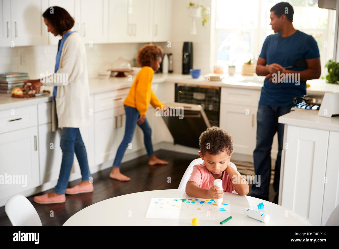 Kleinkind junge Malerei an einem Tisch sitzen in der Küche der Malerei ein pciture, seine Familie im Hintergrund beschäftigt Stockfoto