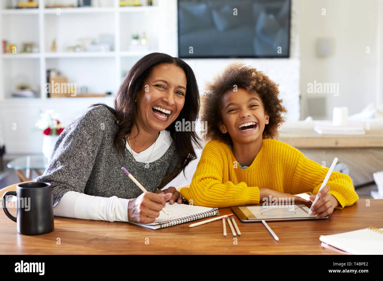 Mittleren Alters gemischten Rasse Frau am Tisch sitzen in Ihrem Esszimmer Zeichnung mit ihr vor - jugendlich Enkelin, in die Kamera lachen, Vorderansicht, in der Nähe Stockfoto