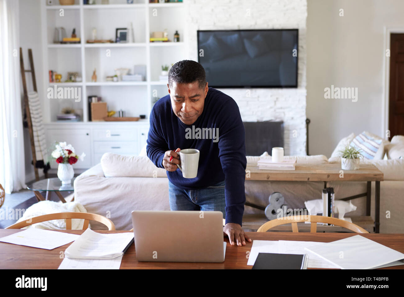 Tausendjährige Hispanic Mann steht auf Tisch im Speisesaal holding Cup und an seinem Laptop Stockfoto