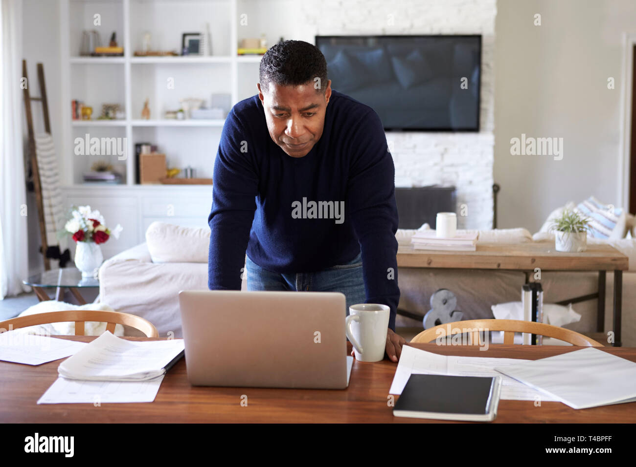 Tausendjährige Hispanic Mann steht auf Tisch im Esszimmer Blick nach unten an seinem Laptop Stockfoto