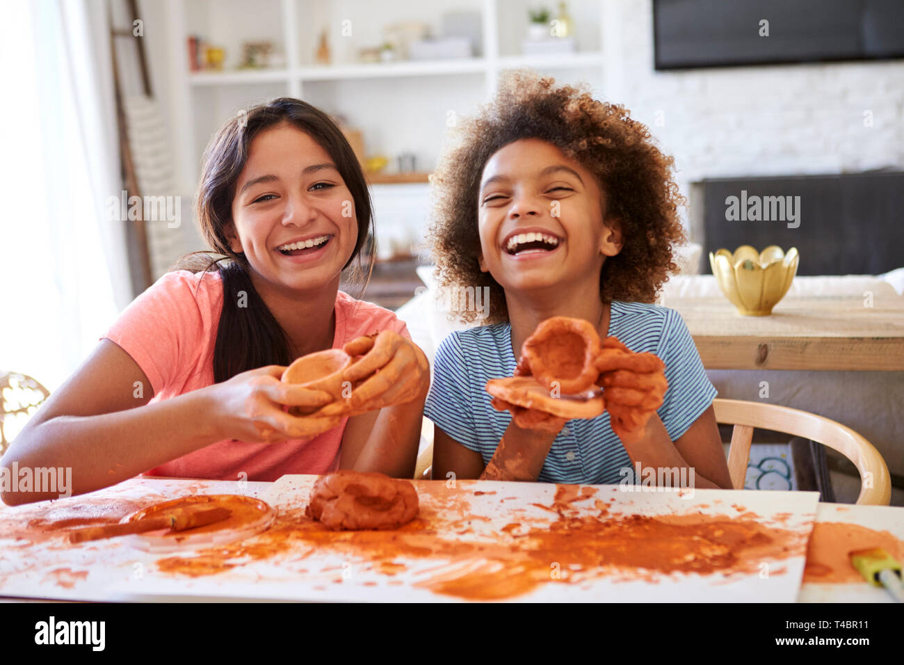 Zwei Freundinnen Spaß spielen mit Knetmasse zu Hause, Lachen und ihre Kreationen zeigen, Kamera, Vorderansicht, in der Nähe Stockfoto