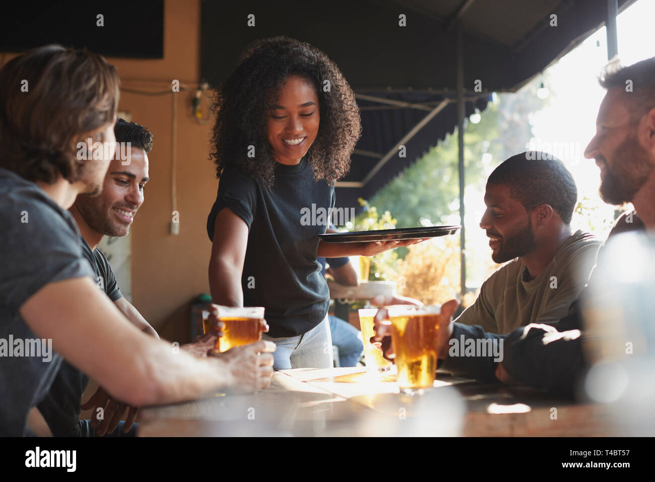 Kellnerin mit Getränken zu Gruppe der männlichen Freunde treffen in Sports Bar Stockfoto