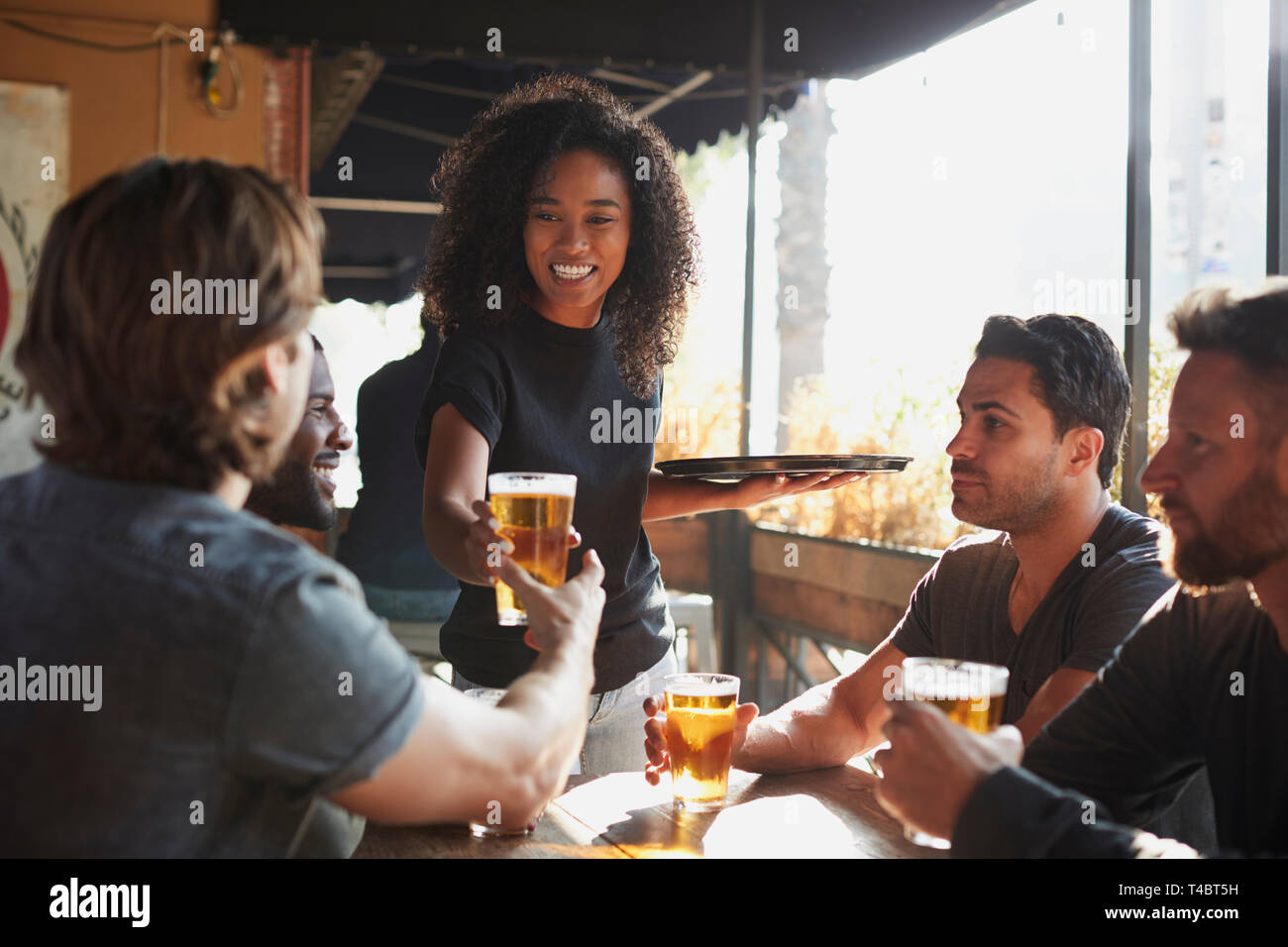 Kellnerin mit Getränken zu Gruppe der männlichen Freunde treffen in Sports Bar Stockfoto