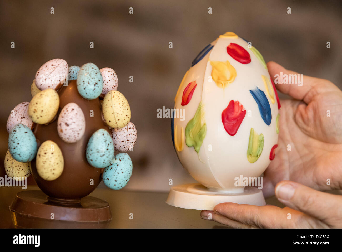 16 April 2019, Bayern, Schweinfurt: Ostereier aus Schokolade in verschiedenen Farben und Darstellungen werden auf einem Tisch in der Chocolaterie Molina, eine Schokoladenfabrik. Ostern ist auch ein Festival für die Süßwarenindustrie. Aber Schokolade Hersteller haben bis zu den gestiegenen Anforderungen der Verbraucher zu Gesicht. (Dpa: "Schokolade Hersteller zwischen Tradition und Trends"). Foto: Daniel Karmann/dpa Stockfoto