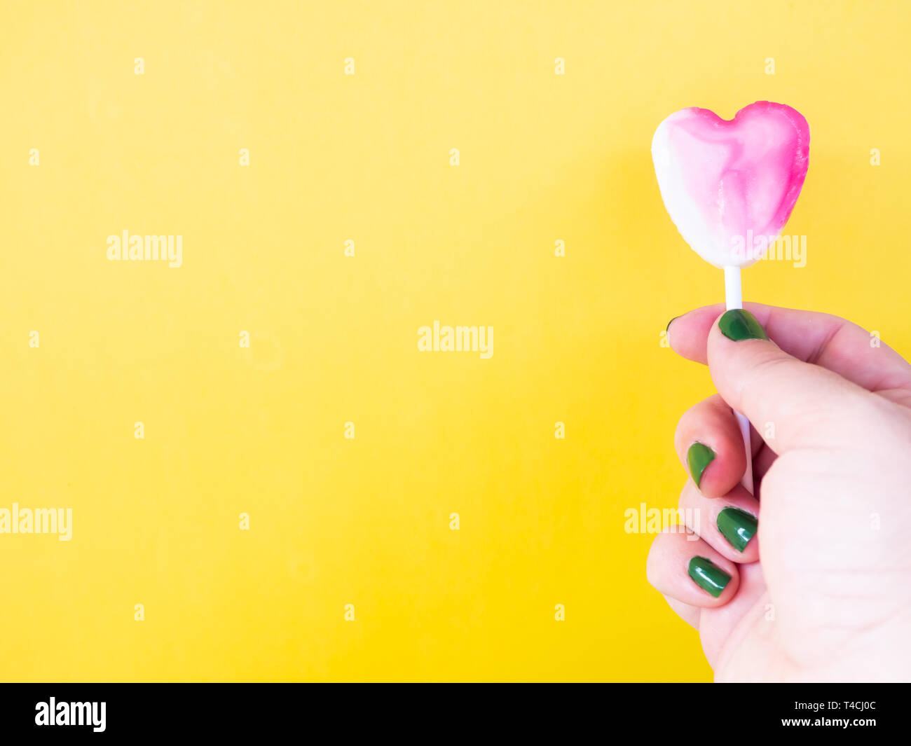 Eine Frau mit grün lackierten Nägel mit einem Lutscher in der Hand und gelbem Hintergrund Stockfoto