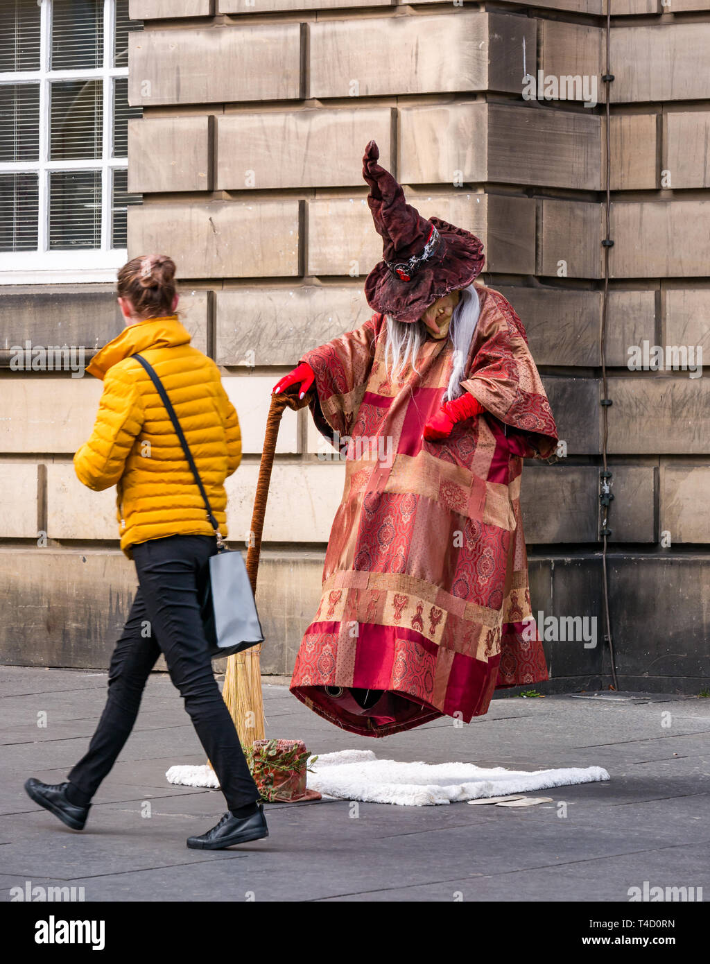 Frau vorbei gehen. Hexe und Besen levitation Street Performer lebende Statue handeln, Royal Mile, Edinburgh, Schottland, Großbritannien Stockfoto
