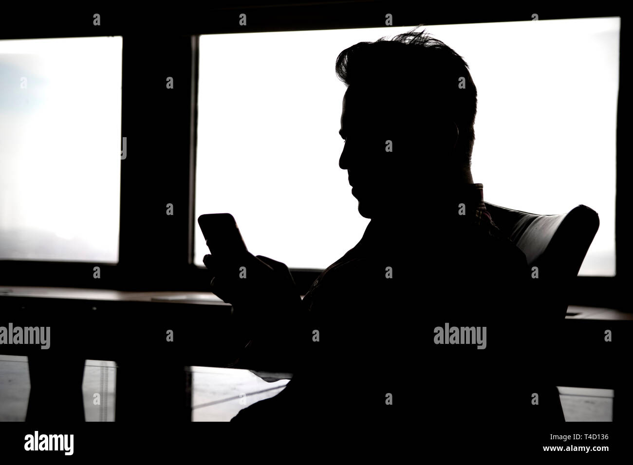 Schwarze Silhouette des Mannes am Tisch, an Handy Gerät suchen. Stockfoto