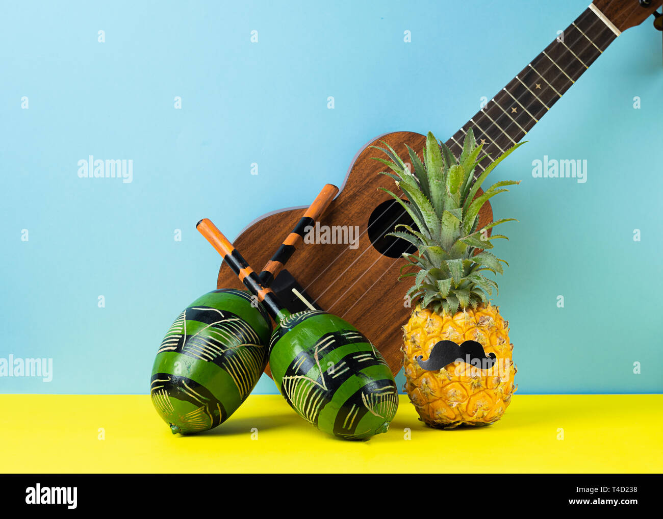 Lustig kostümierte Ananas mit schwarzen Schnurrbart, ukulele Maracas blau  gelben Hintergrund. Das Konzept Urlaub Musik Party Stockfotografie - Alamy