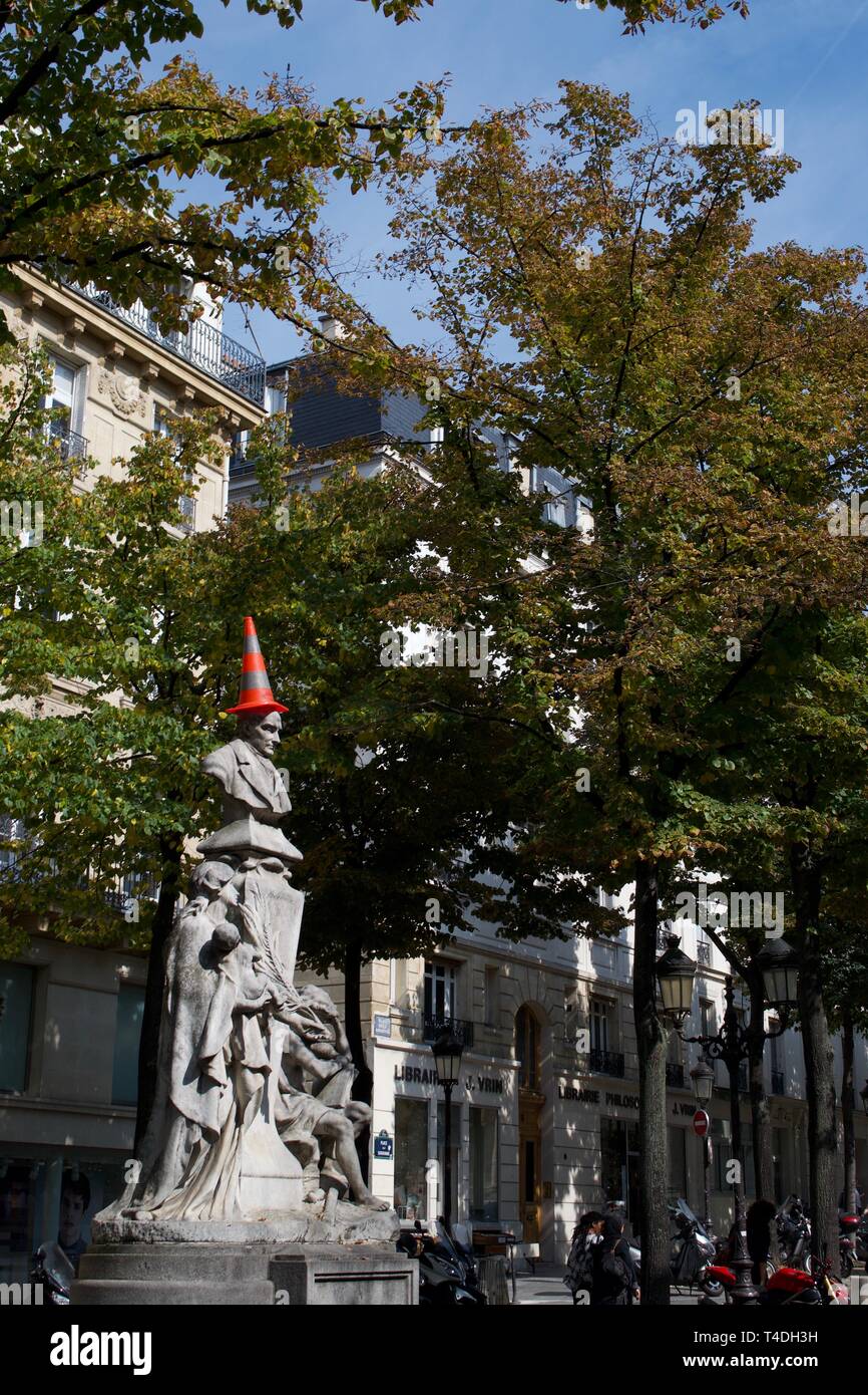 Eine Statue auf der Place de la Sorbonne, Paris, Frankreich. Stein Statue eines Mannes, unter Bäumen vor den Gebäuden. Ein Rot und Silber/Grau gestreifte Verkehr con Stockfoto