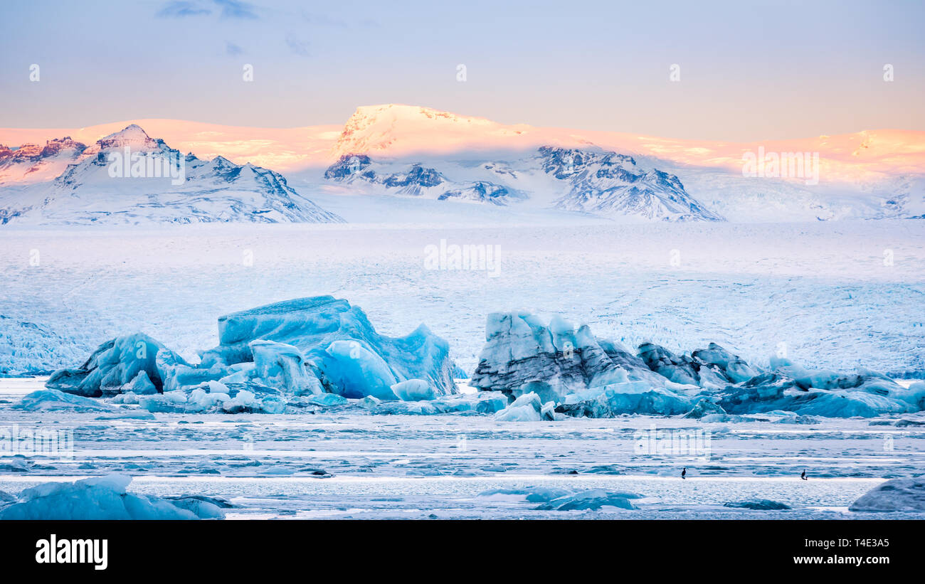 Eisberge schwimmen auf Gletschersee Jökulsárlón Gletscherlagune bei Sonnenaufgang, mit Hintergrund Berggipfel von Sunrise beleuchtet, in Island. Stockfoto