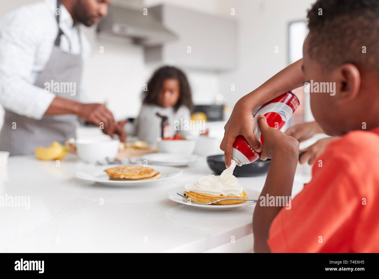 Junge hinzufügen Creme zu Pfannkuchen als Familie genießen Sie Ihr Frühstück in der Küche zu Hause zusammen Stockfoto