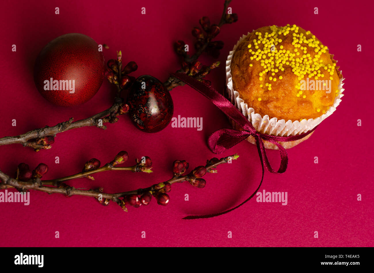 Ostern Muffin mit Schleife dekoriert und besprüht, gefärbte Eier und ein Zweig der Aprikosenbaum auf dunklem Rosa oder Pink Hintergrund. Grußkarte. Stockfoto