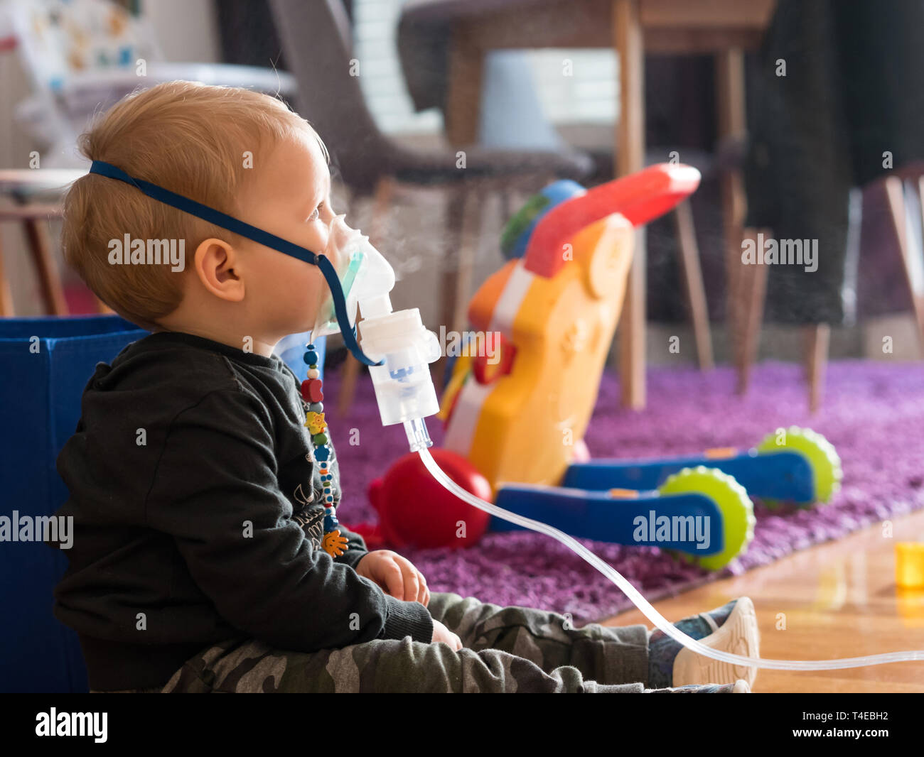 Kleine kaukasischen Kind sitzt auf dem Boden mit Sauerstoff Maske zu Hause einatmen Stockfoto