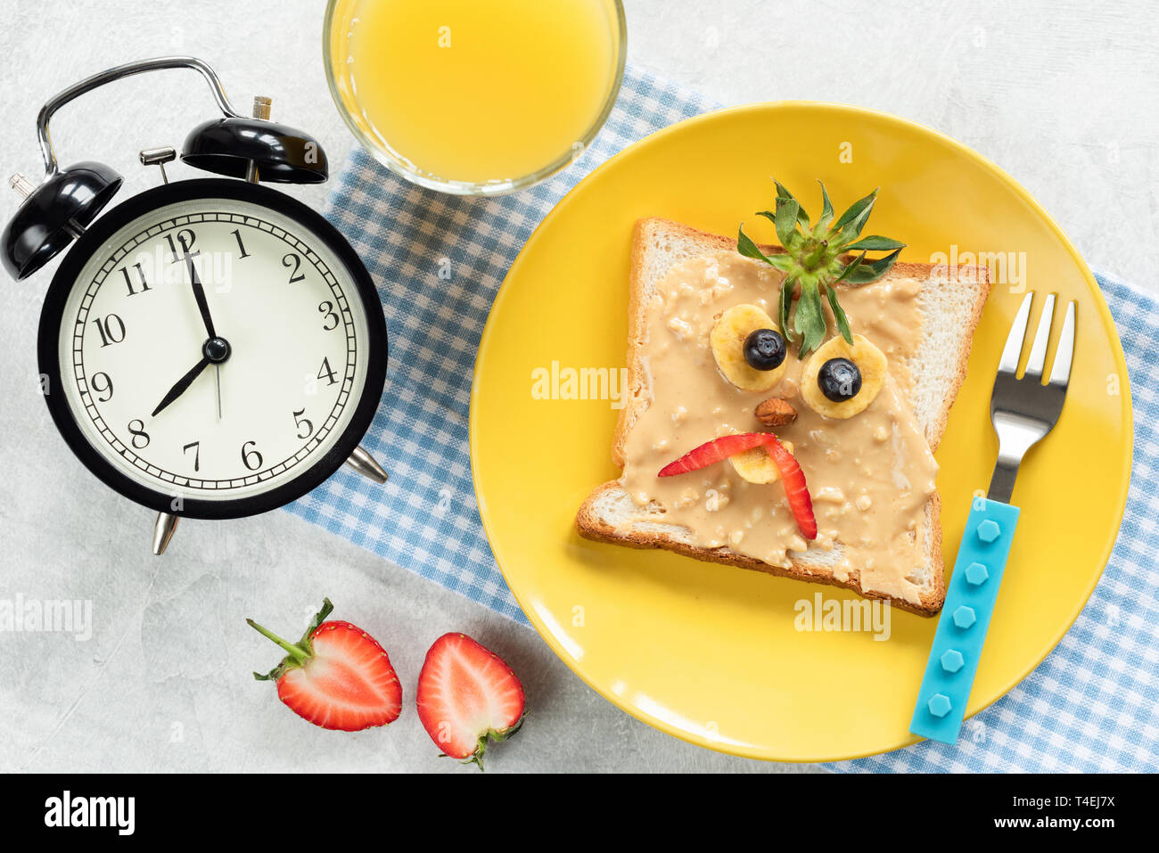 Kinder Frühstück Mahlzeit, Peanut butter Toast mit Funny Face von Angry Vogel oder böse Piraten auf eine trendige gelb Platte. Glas Orangensaft und Uhren auf s Stockfoto