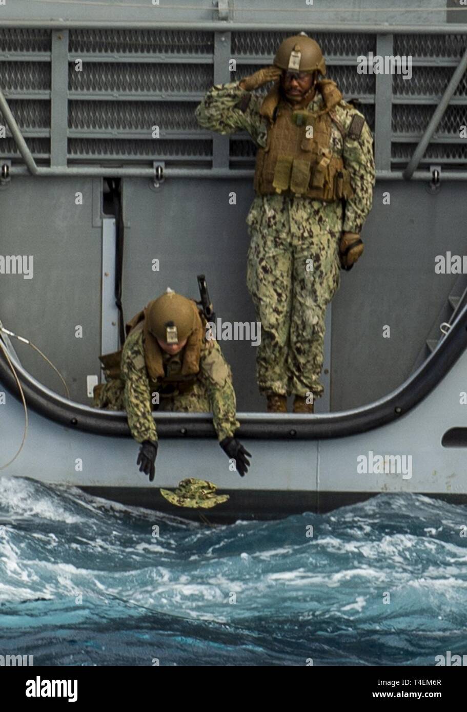 SANTA Rita, Guam (29. März 2019). Engineman Feuerwehrmann Guadalupe Garcia, von Bakersfield, Kalifornien, (links) legt einen "boonie Cap", während der Vietnam Krieg Gedenkveranstaltung an Bord ein Mark VI Patrouillenboot während Chief Quartermaster Stephan kühlt, aus Brooklyn, NY, ehrt rendert, vor einem Feuer. Die "boonie Cap "Vordergrund während des Vietnam Krieges bei der US Armee Grünhelme begann, tragen Sie im Feld zusammen mit Australischen und Armee der Republik Vietnam. Küsten Riverine Squadron (CRS) 2 Det. Guam, an die in den Küstenzonen Riverine Gruppe 1, Det zugeordnet. Guam, ist in der Lage, con Stockfoto