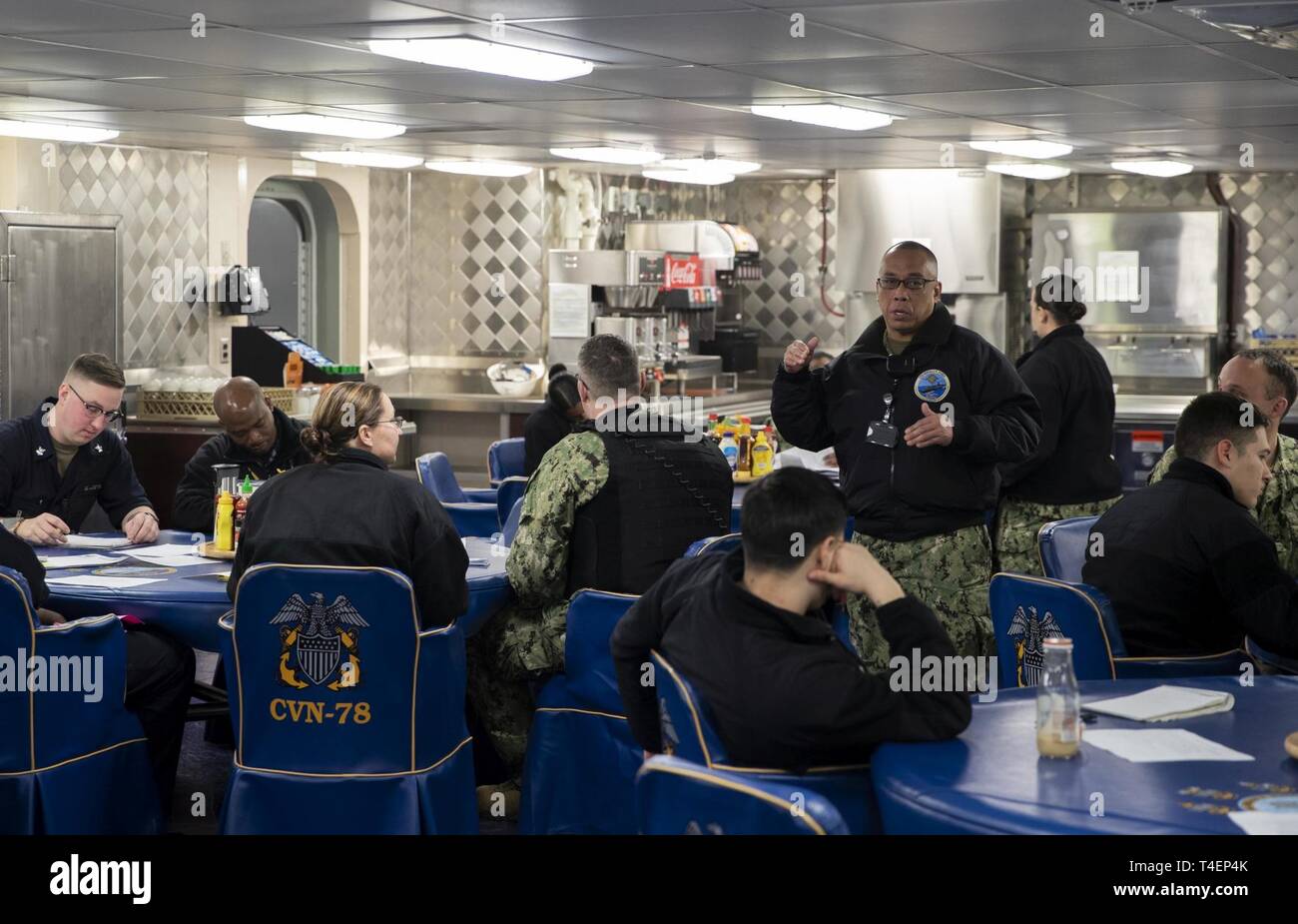 NEWPORT NEWS, Virginia (2. April 2019) Chief Warrant Officer Felipe Tubera, USS Gerald R. Ford's (CVN 78) Food Service Officer, Adressen Segler während einer Supply Abteilung Services Board auf Ford's Chaos Decks überprüfen. Ford wird derzeit in post-shakedown Verfügbarkeit Huntington Ingalls Industries-Newport Nachrichten Schiffbau. Stockfoto