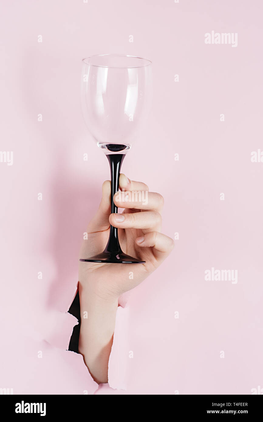 Kreative Bilder von weiblichen Hand hält Wein Glas durch ein Loch in rosa Papier gesehen wird. Hellen Hintergrund und eine Lücke Schlitz in dem Papier. Urlaub Stockfoto