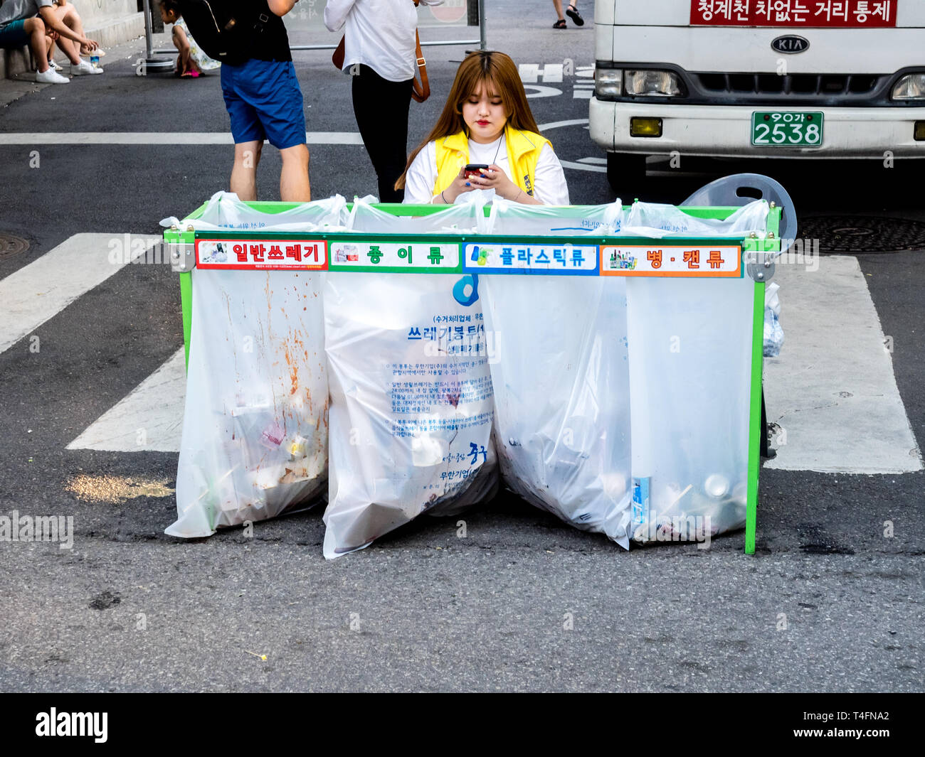 Seoul, Südkorea - 17. Juni 2017: Frau sitzt in der Nähe von abfalltrennung Container mit farbigen Inschriften für Kunststoff, Glas Flaschen und Papier. Stockfoto
