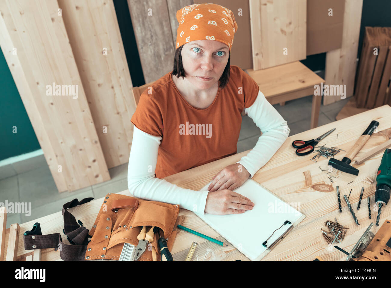 Portrait von selbständigen weiblichen Tischler tragen bandanna am Schreibtisch in Ihrem Holzarbeiten Workshop durch verschiedene Tools des Handels umgeben Sitzen Stockfoto