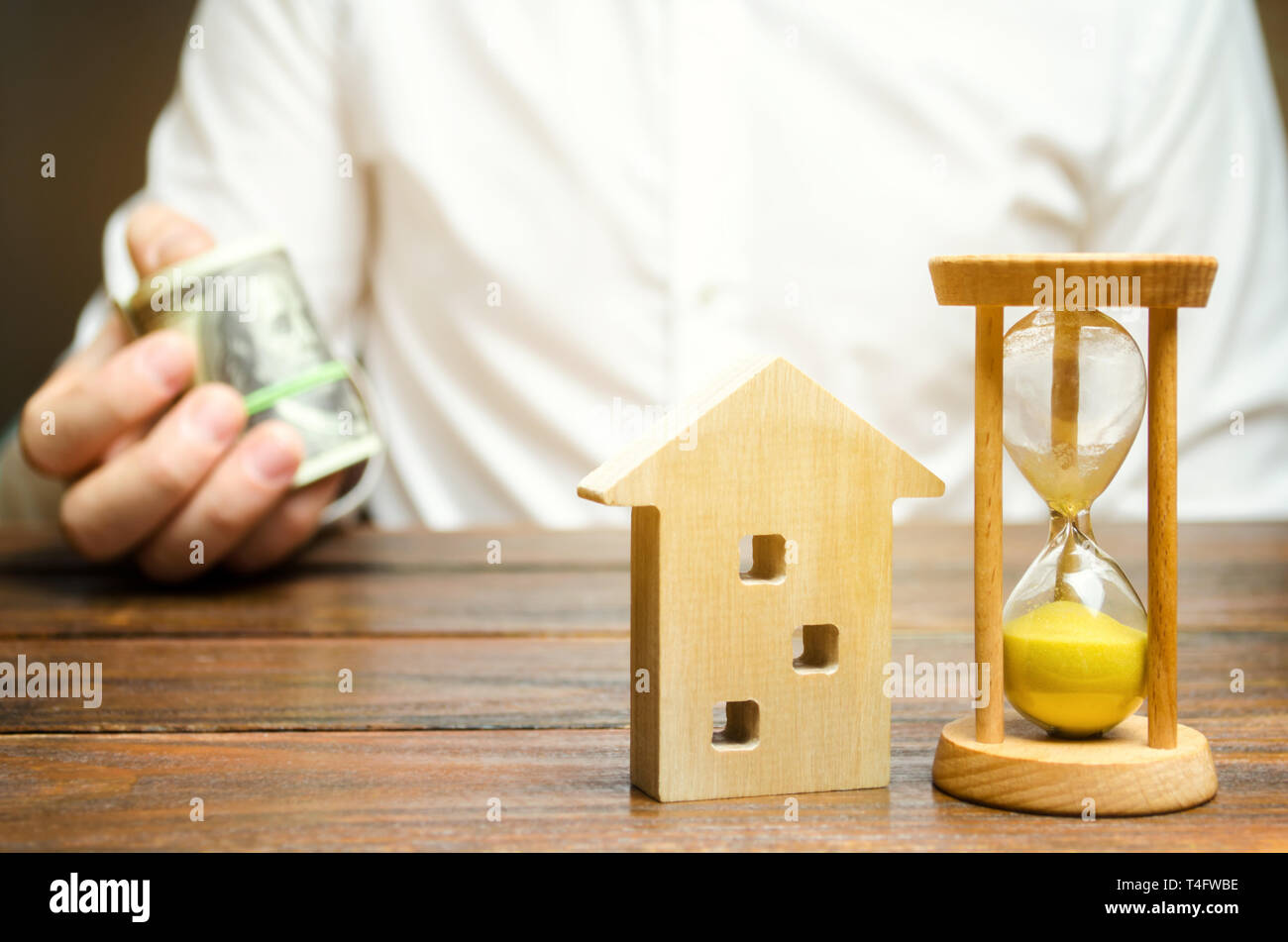 Holz- Haus und die Uhr. Unternehmer hält Geld. Die Zahlung der Anzahlung oder Vorauszahlung für die Miete ein Haus oder eine Wohnung. Langfristige Hypothek auf das Haus Stockfoto