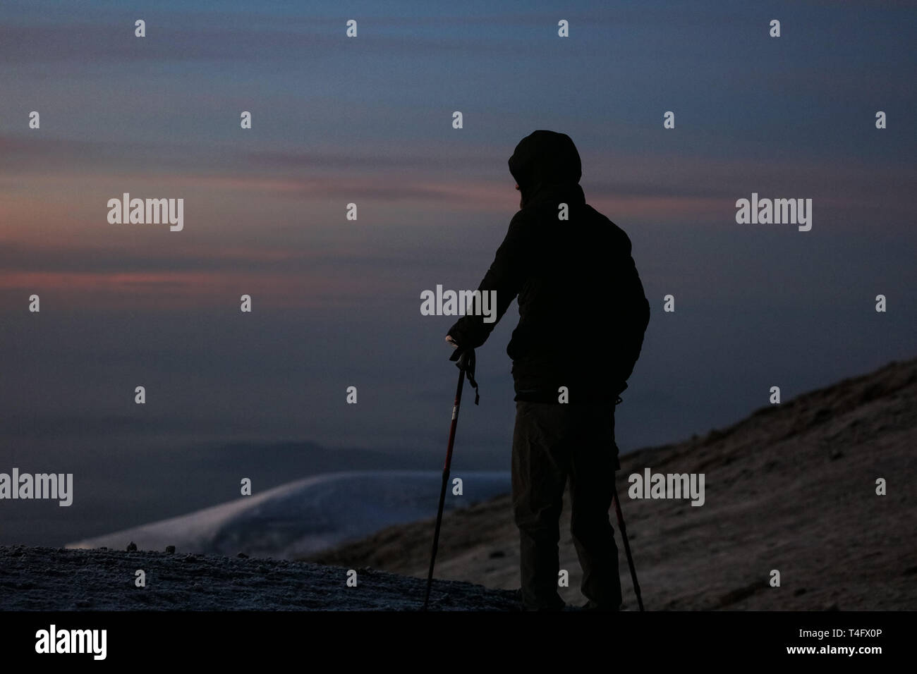 Mann im schwarzen Sportswear steht auf dem Gipfel des Kilimanjaro in Afrika. Genießt die schöne Aussicht auf die Berge auf den Sonnenaufgang. High Peaks Stockfoto