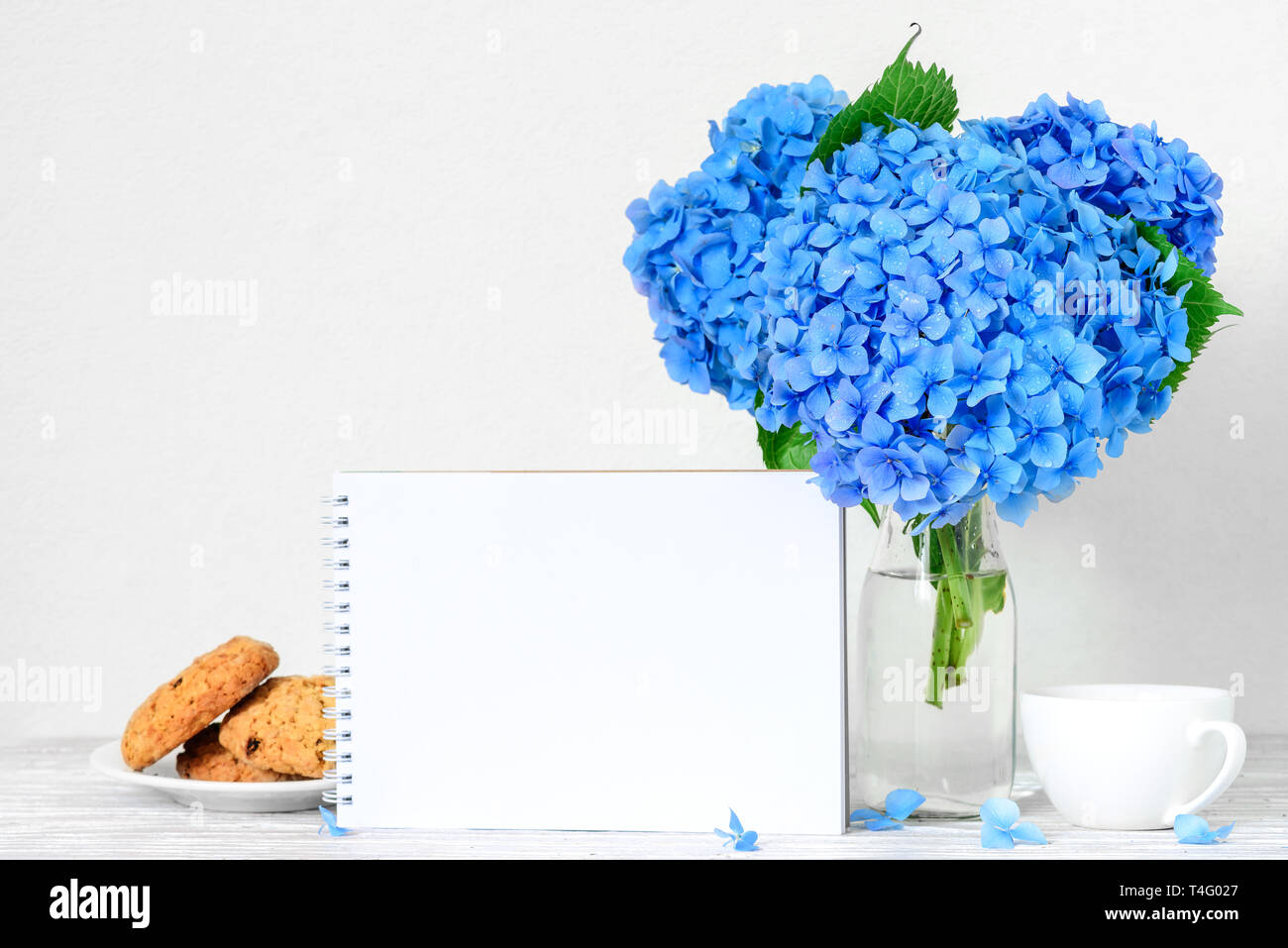 Stillleben mit Blumenstrauß der Blaue Hortensie Blumen, leere Grußkarte, Tasse Kaffee und Cookies. Mock up. Urlaub oder Hochzeit Hintergrund Stockfoto