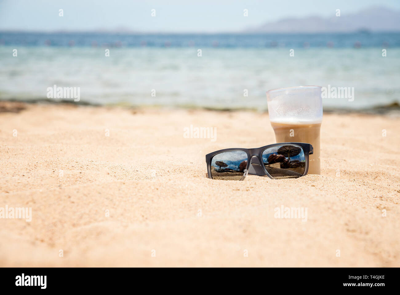 Sonnenbrille und Glas auf dem Sand in der Nähe des Meeres Stockfoto