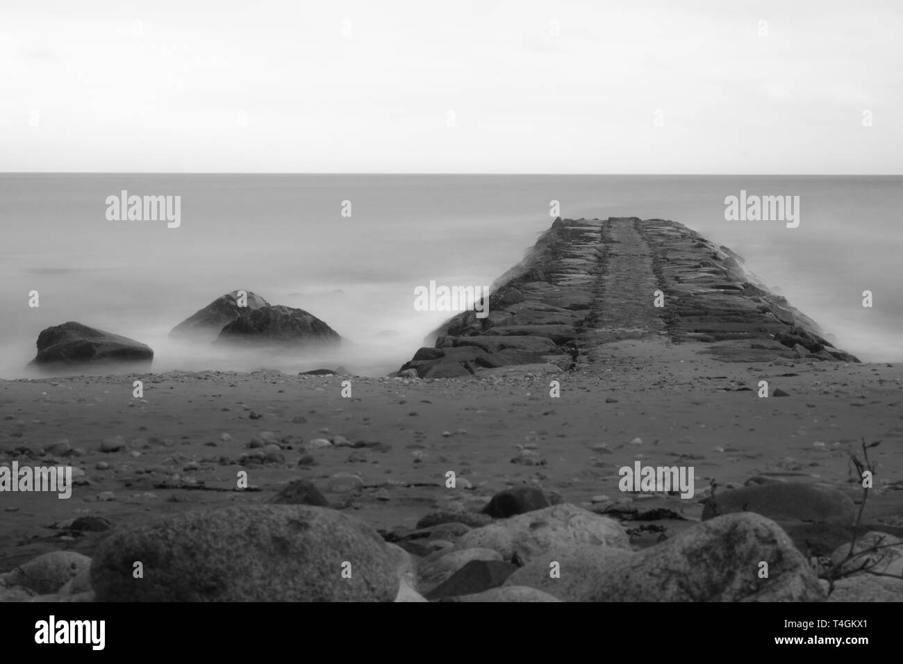 Verträumt lange Belichtung in Schwarz und Weiß, aus einem felsigen Strand und Steg auf den Horizont gerichtet, Block Island, Rhode Island Stockfoto